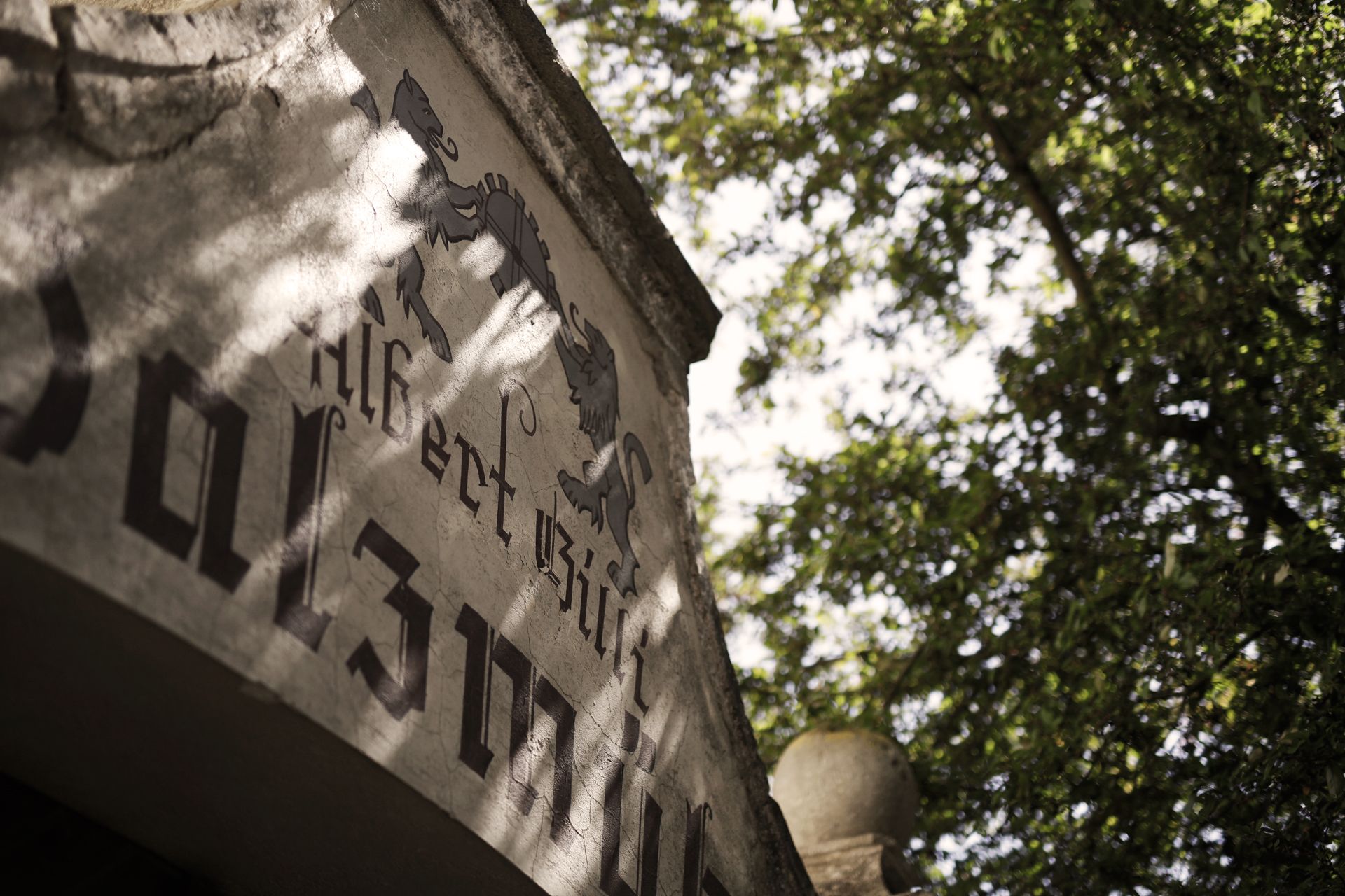 Close-up of an old building with lettering and coat of arms, surrounded by trees.