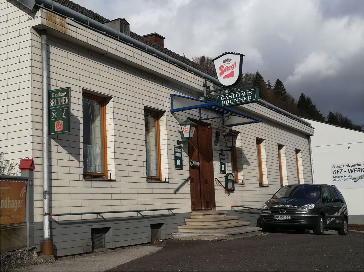 Exterior view of the traditional Brunner inn with shingled, white façade and Stiegl sign