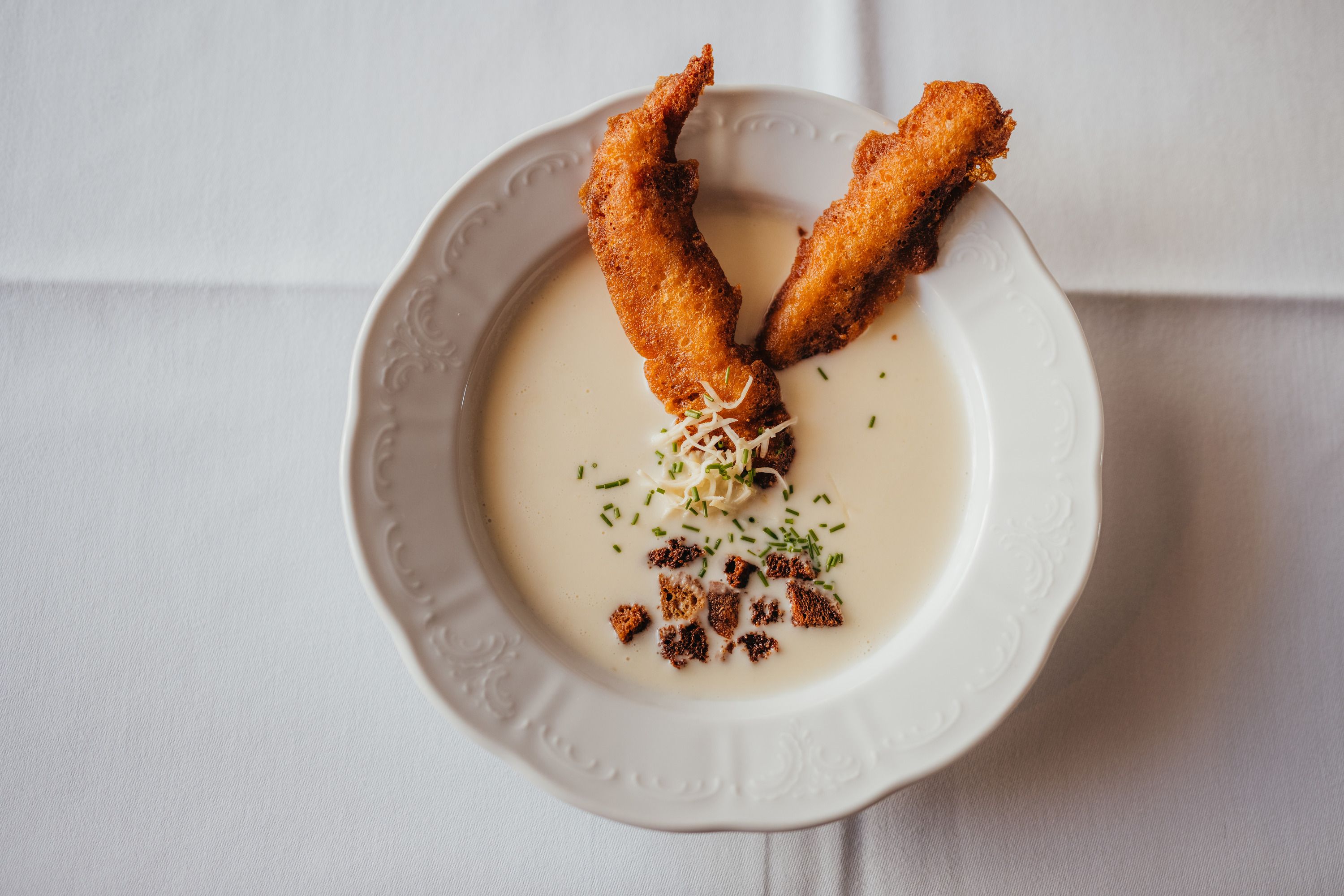 Creamy soup with smoked trout strips and herbs on a white plate.