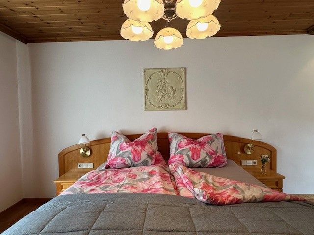 A cozy bedroom with a double bed, floral bedding and a wooden ceiling. A lamp hangs from the ceiling.