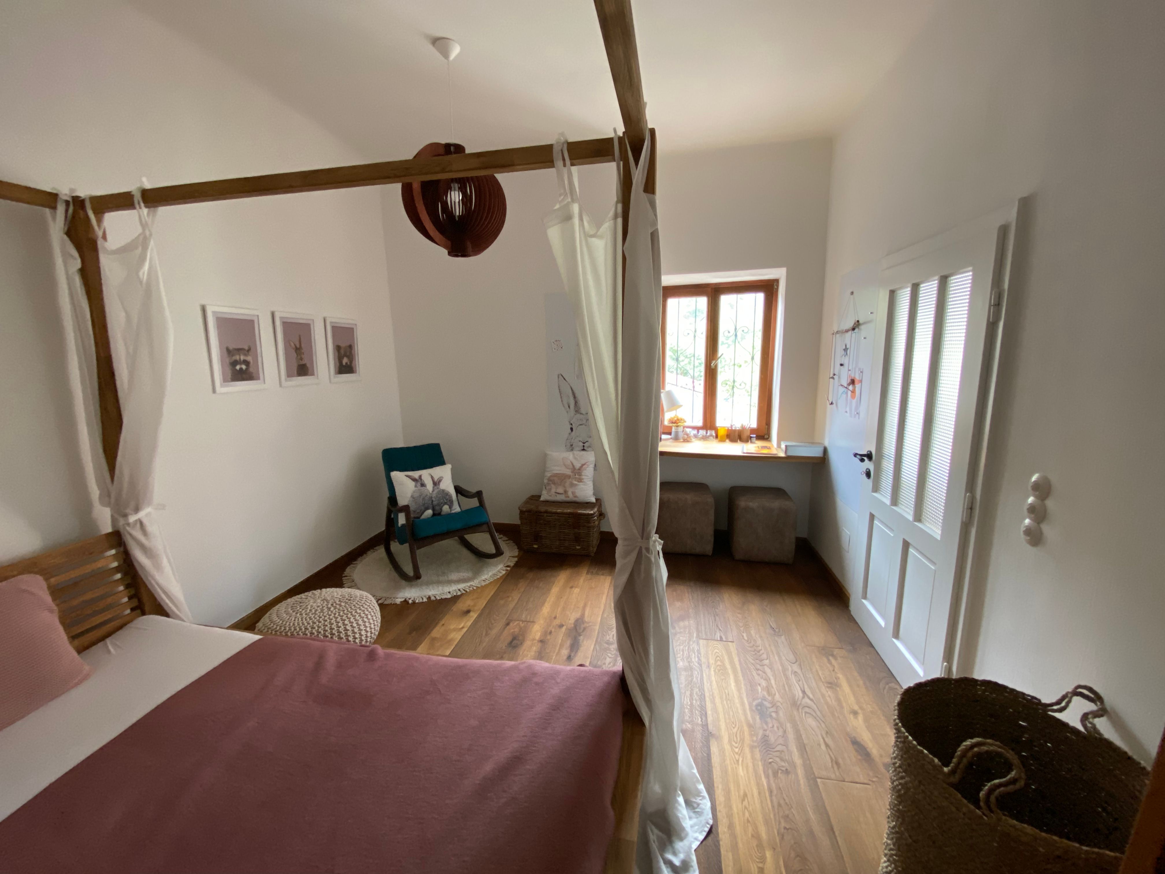 Cozy bedroom with four-poster bed, rocking chair and window seat. Wooden floor and light-colored walls.