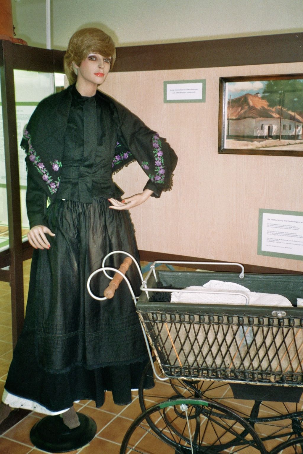 A mannequin in traditional clothing next to an old baby carriage in a showroom.