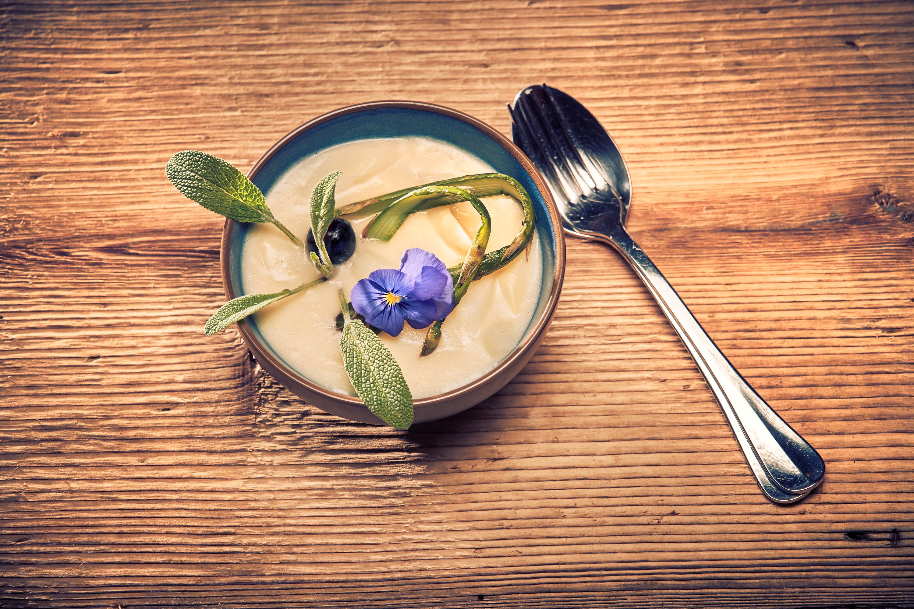 Cream of asparagus soup Soup with blossom and herbs on wooden table, spoon next to it.