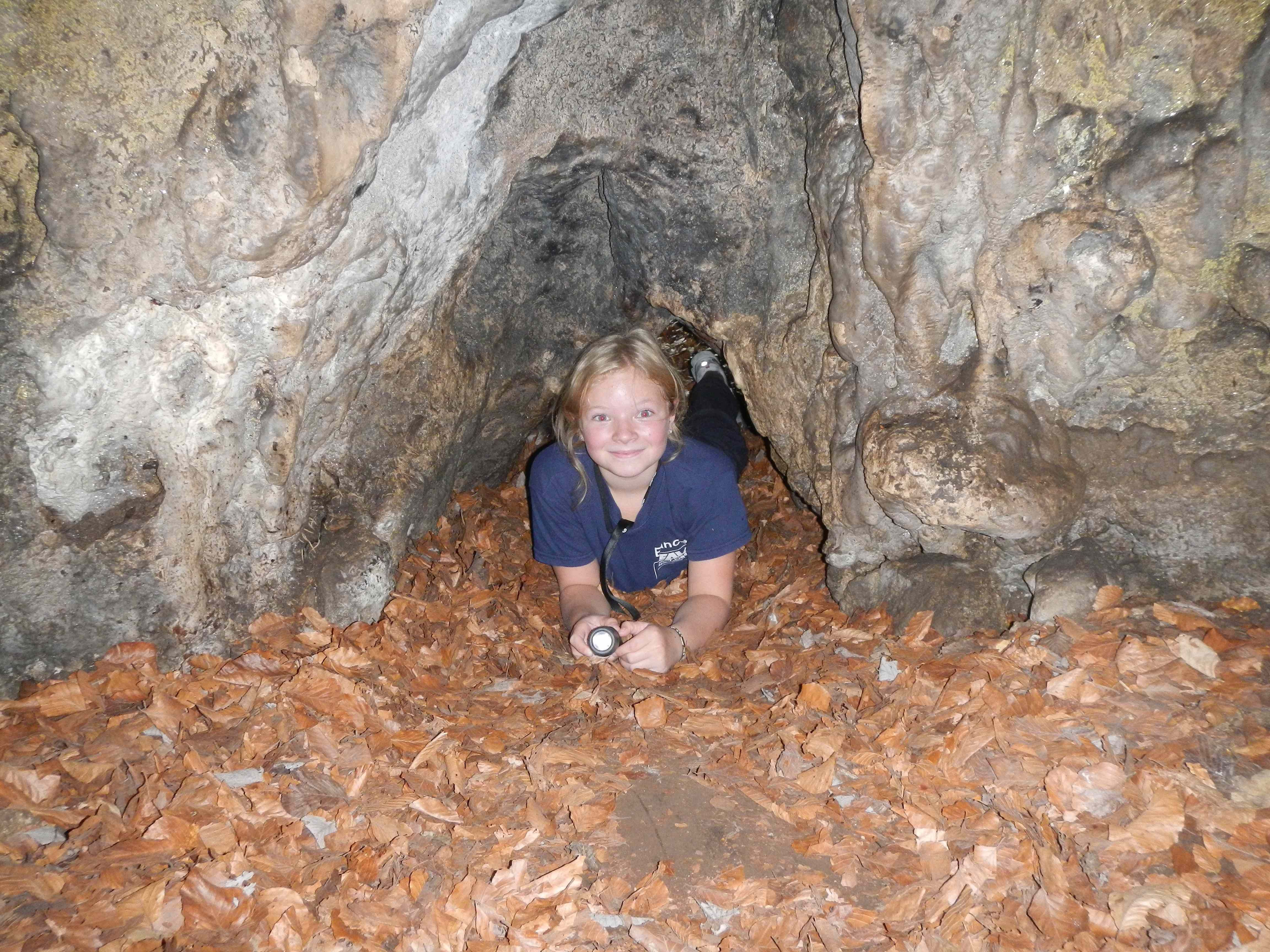 A child lies on leaves in a cave and holds a flashlight.