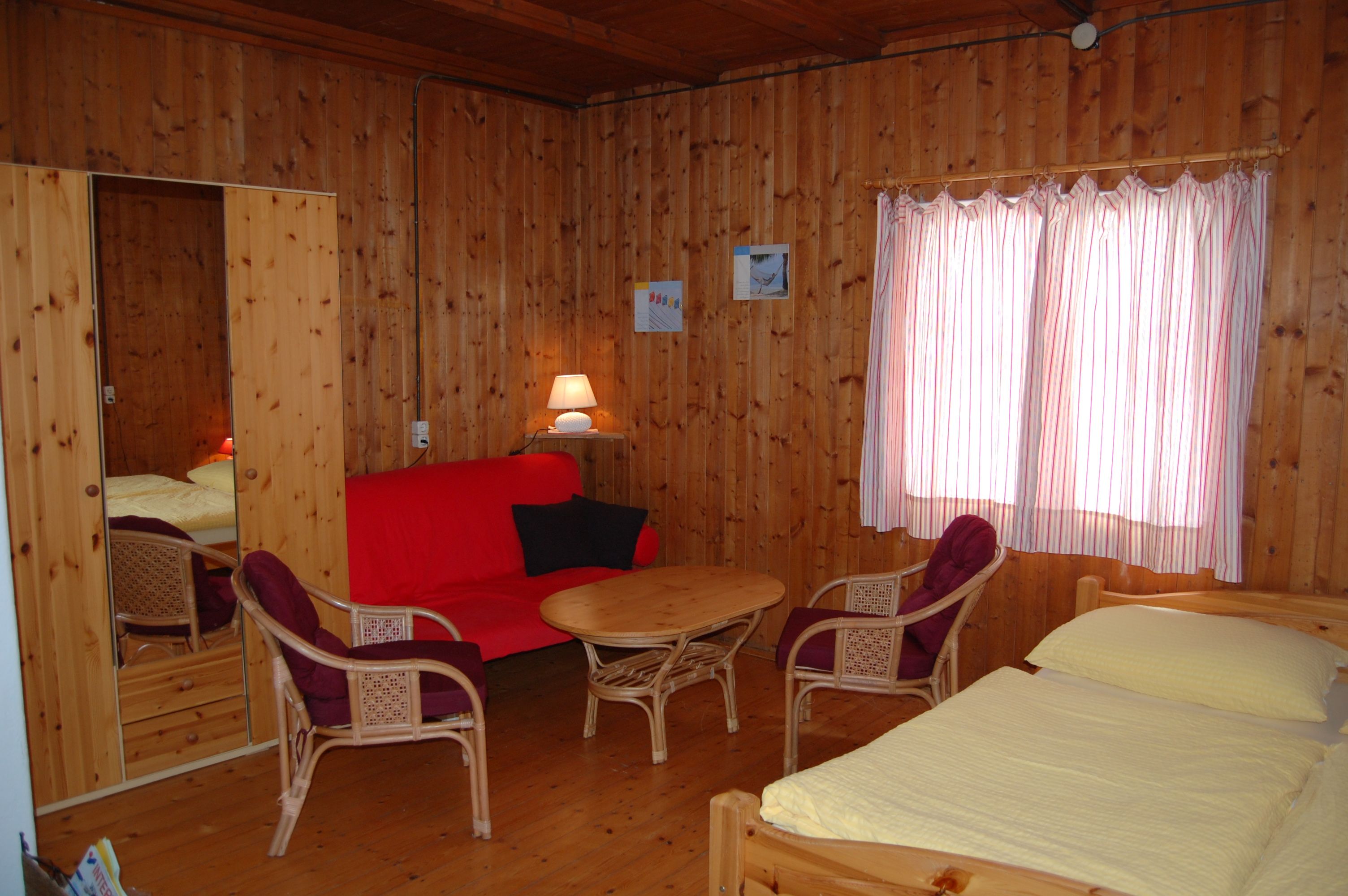 Interior view of a cozy room with wooden walls, red sofa, table, chairs and bed.