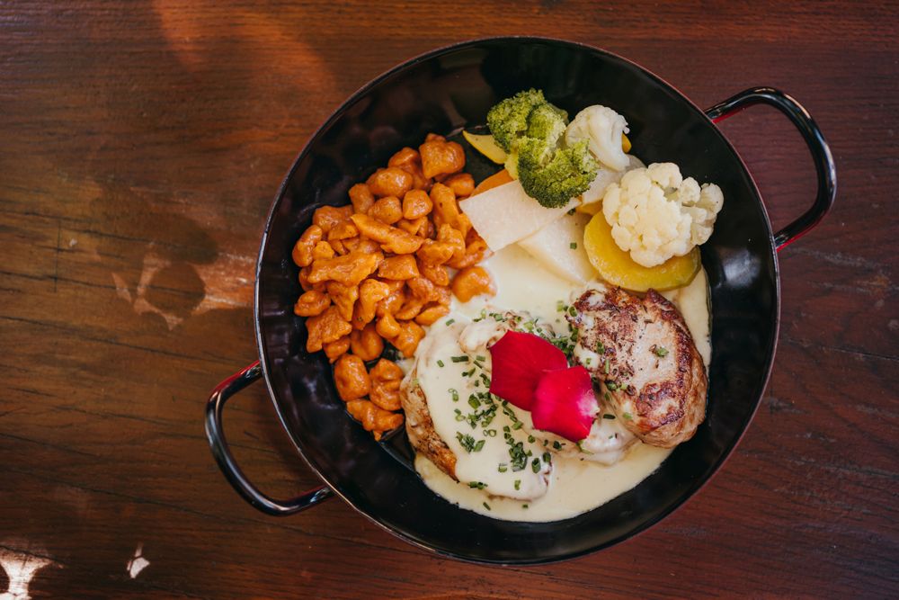 Pork medallions with cheese sauce, red spaetzle and garden vegetables in a black pan.