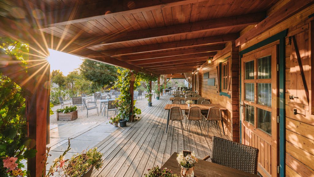 Wooden terrace with tables and chairs, surrounded by plants, at sunset.