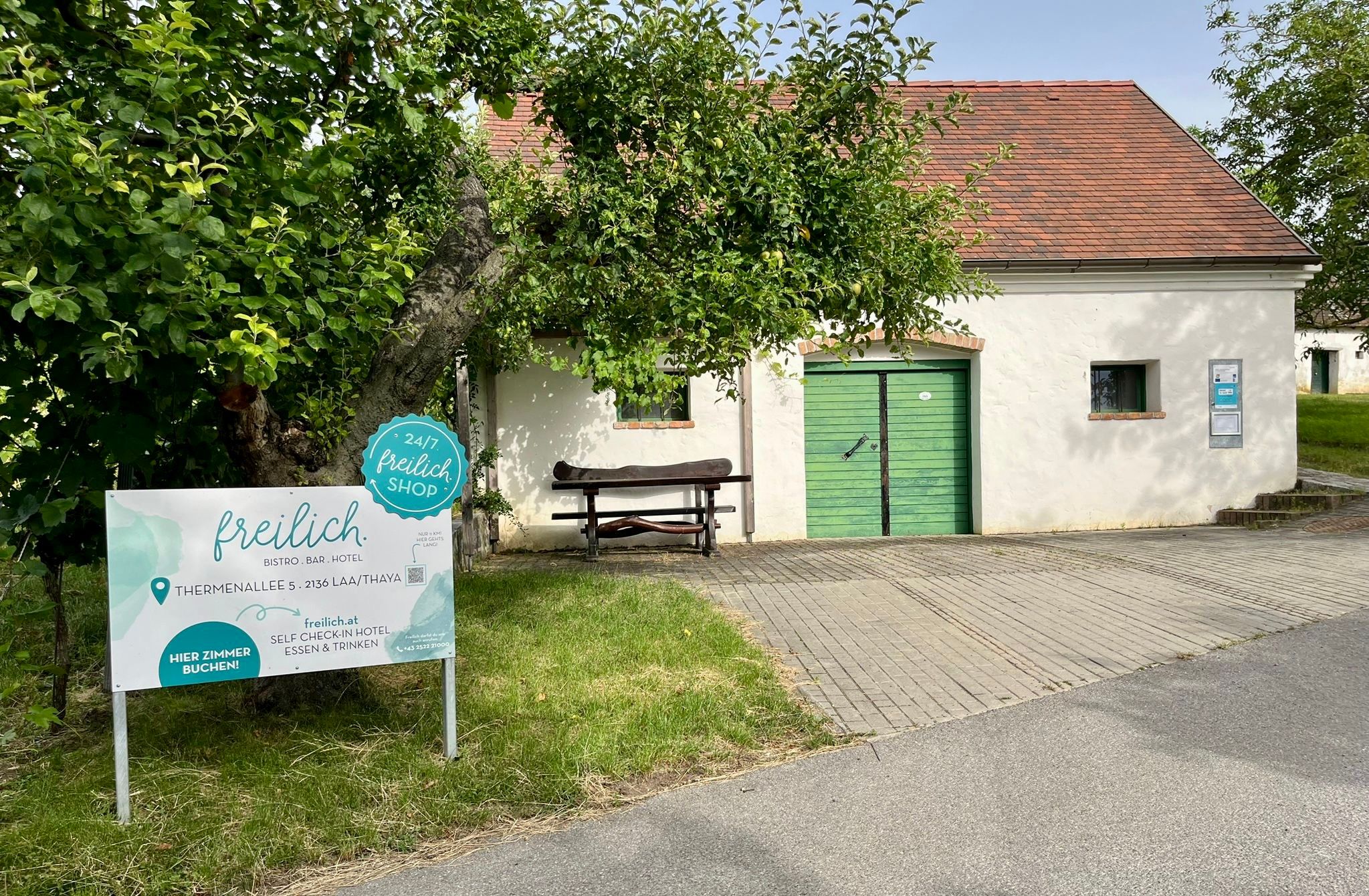 Exterior view of the freilich. building with a green gate, sign, and trees in front of it.