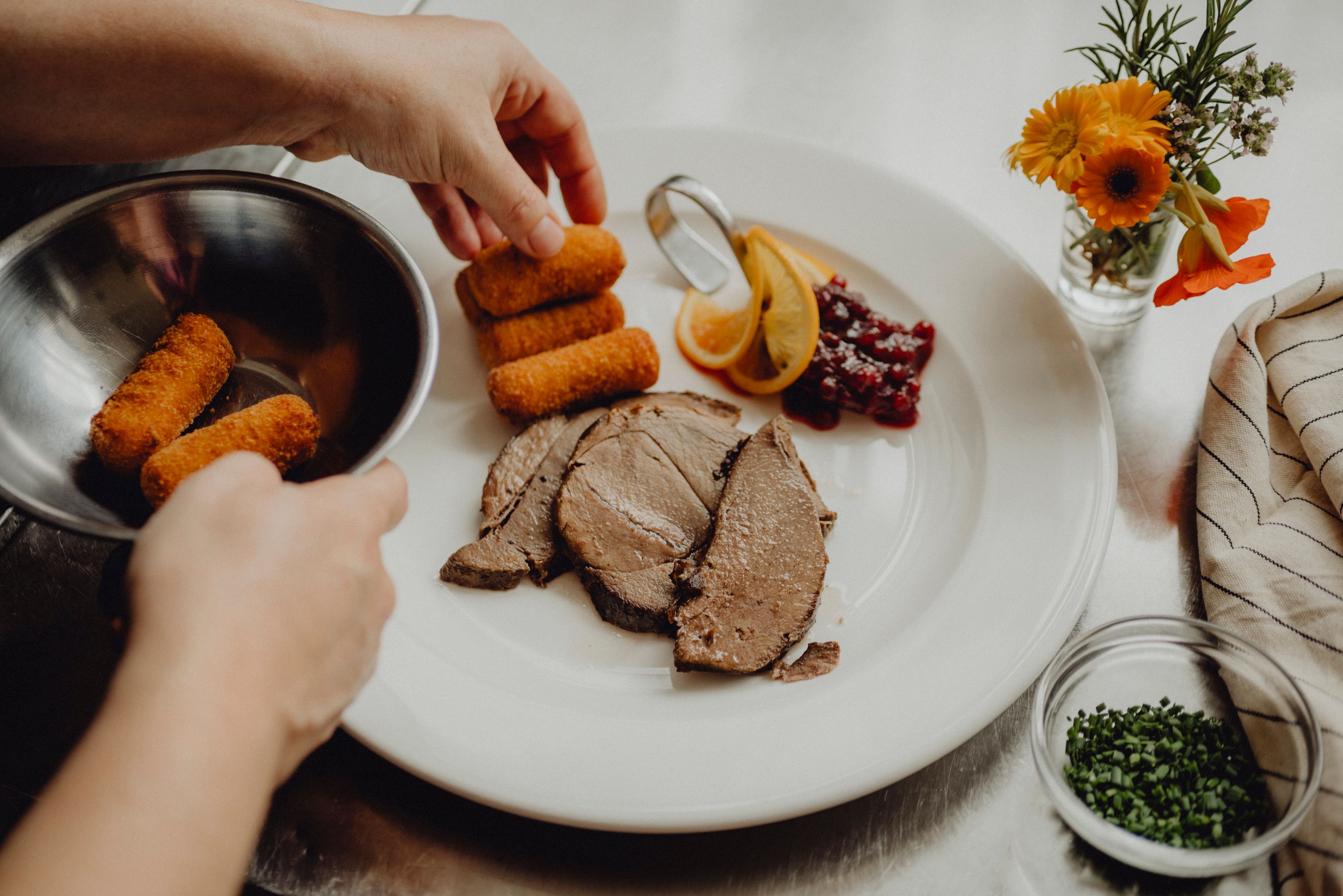 A plate with meat, croquettes, cranberries and lemon slices is served.