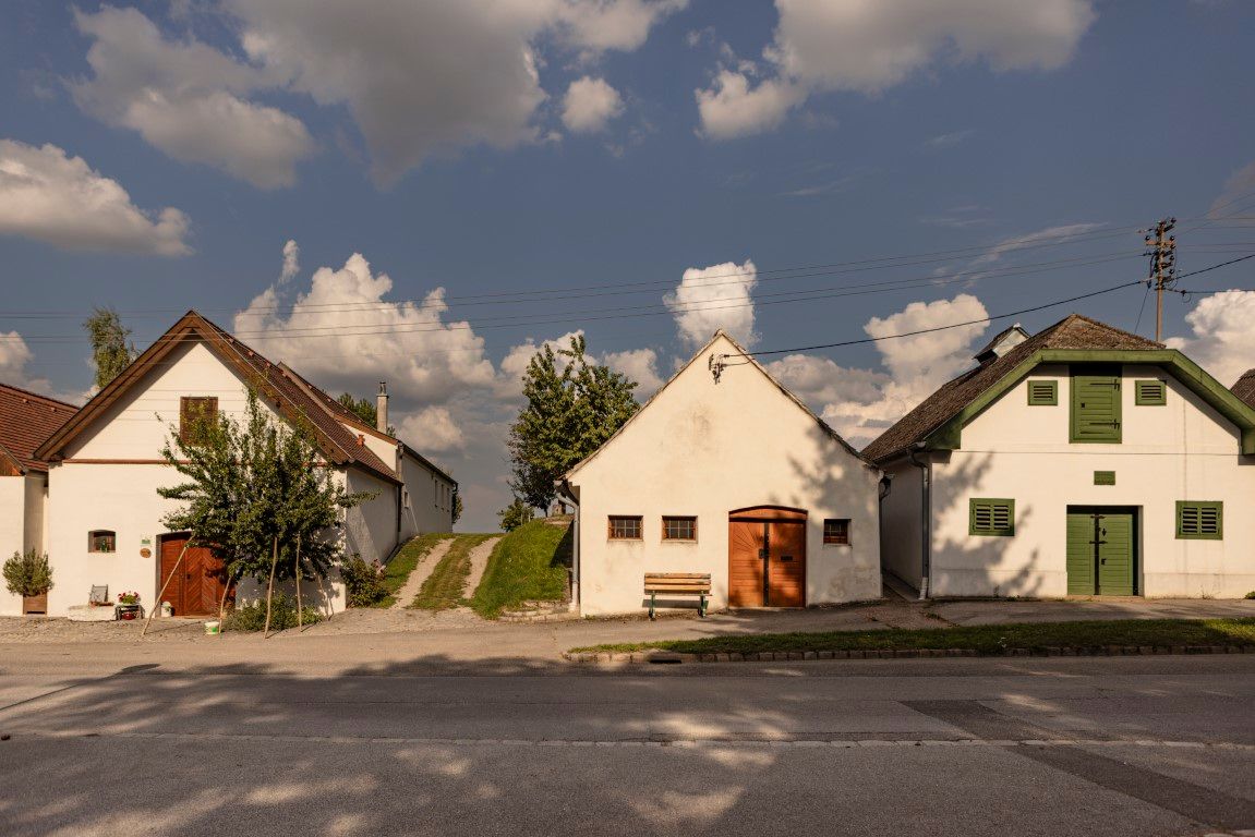 Three traditional cellar houses in Kettlasbrunn under a blue sky with clouds.
