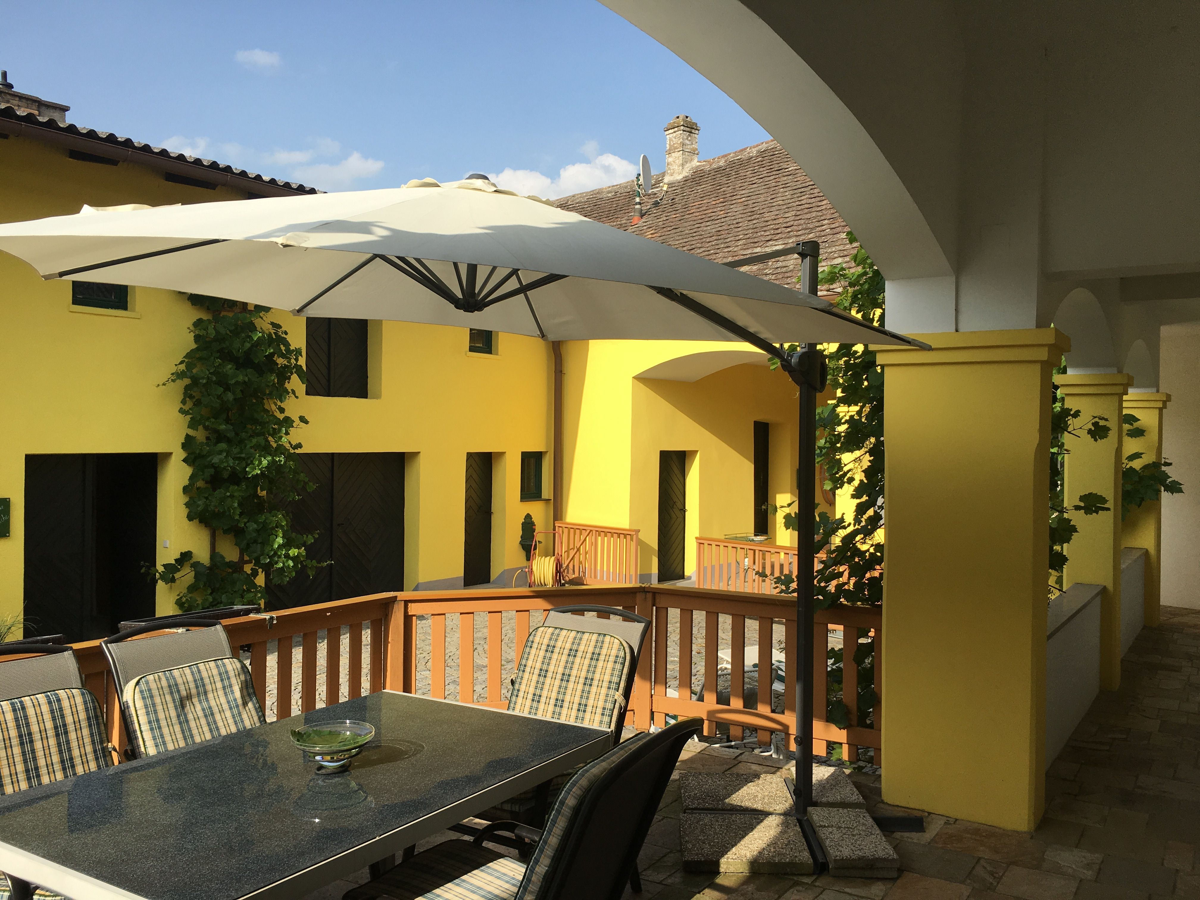 Terrace with table, chairs and parasol in front of yellow building.