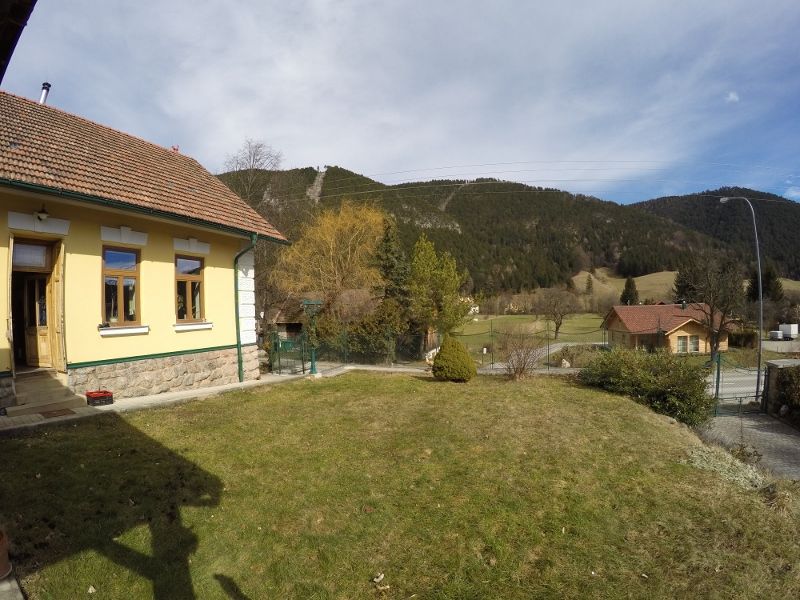 Front garden with yellow house and view of wooded hills.
