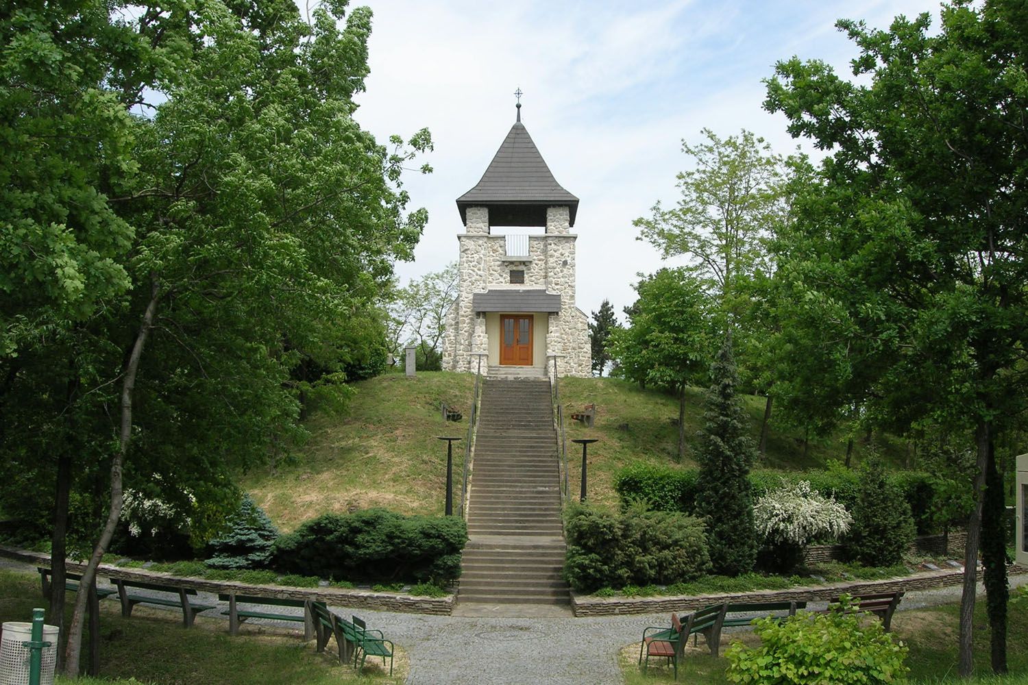 A stone war memorial with a tower and steps, surrounded by trees and benches.