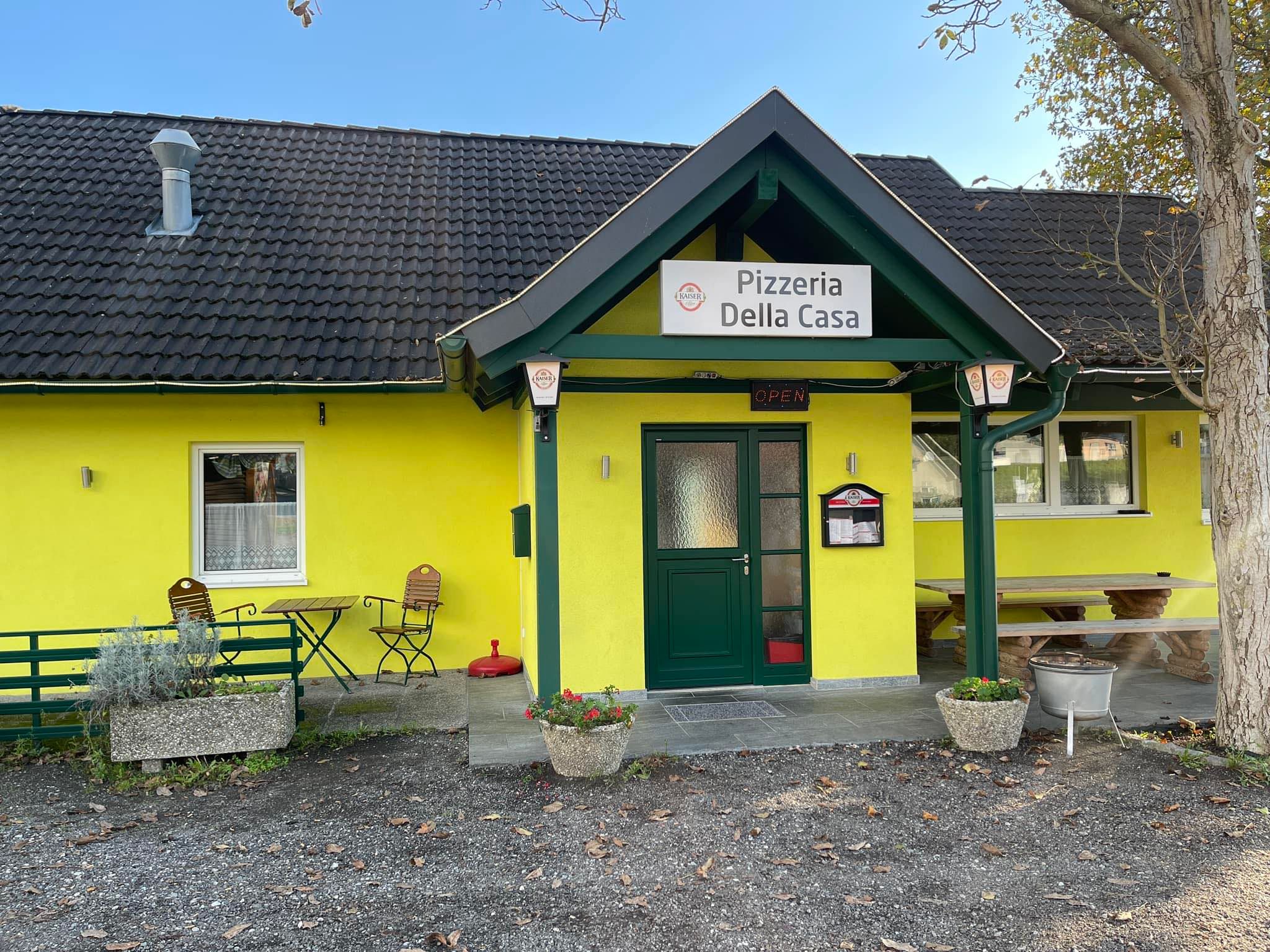 Exterior view of a yellow pizzeria with the name 'Pizzeria Della Casa'.