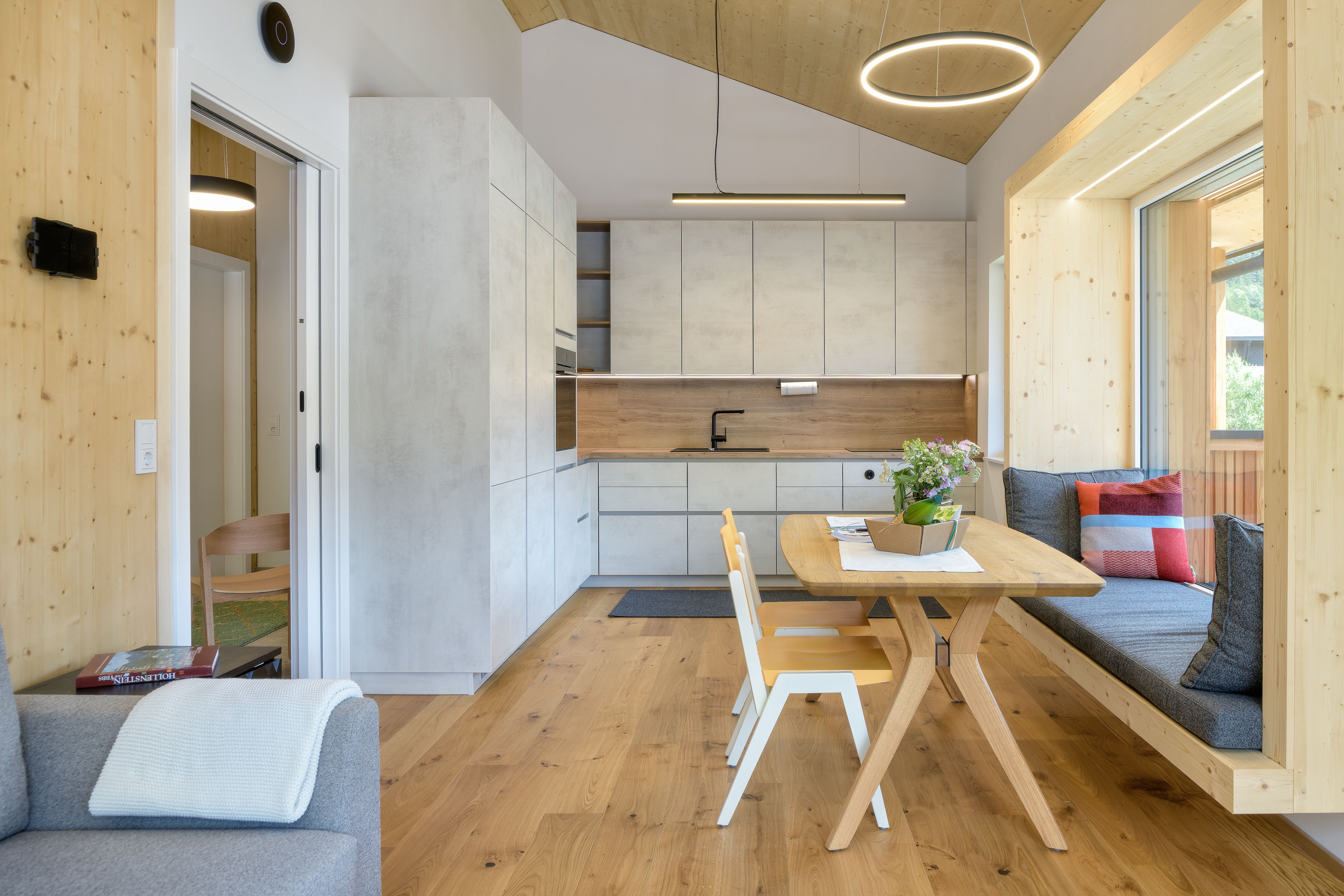 Modern kitchen with a wood- and concrete-look finish, a dining table, and a bench by the window.