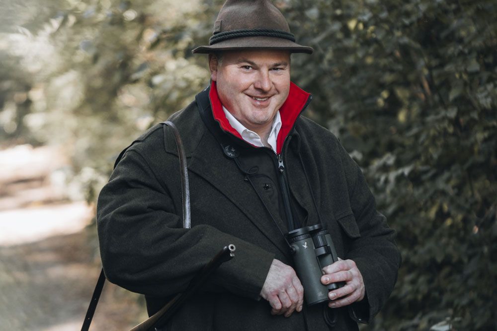 Man in hunting clothes with binoculars in the forest.
