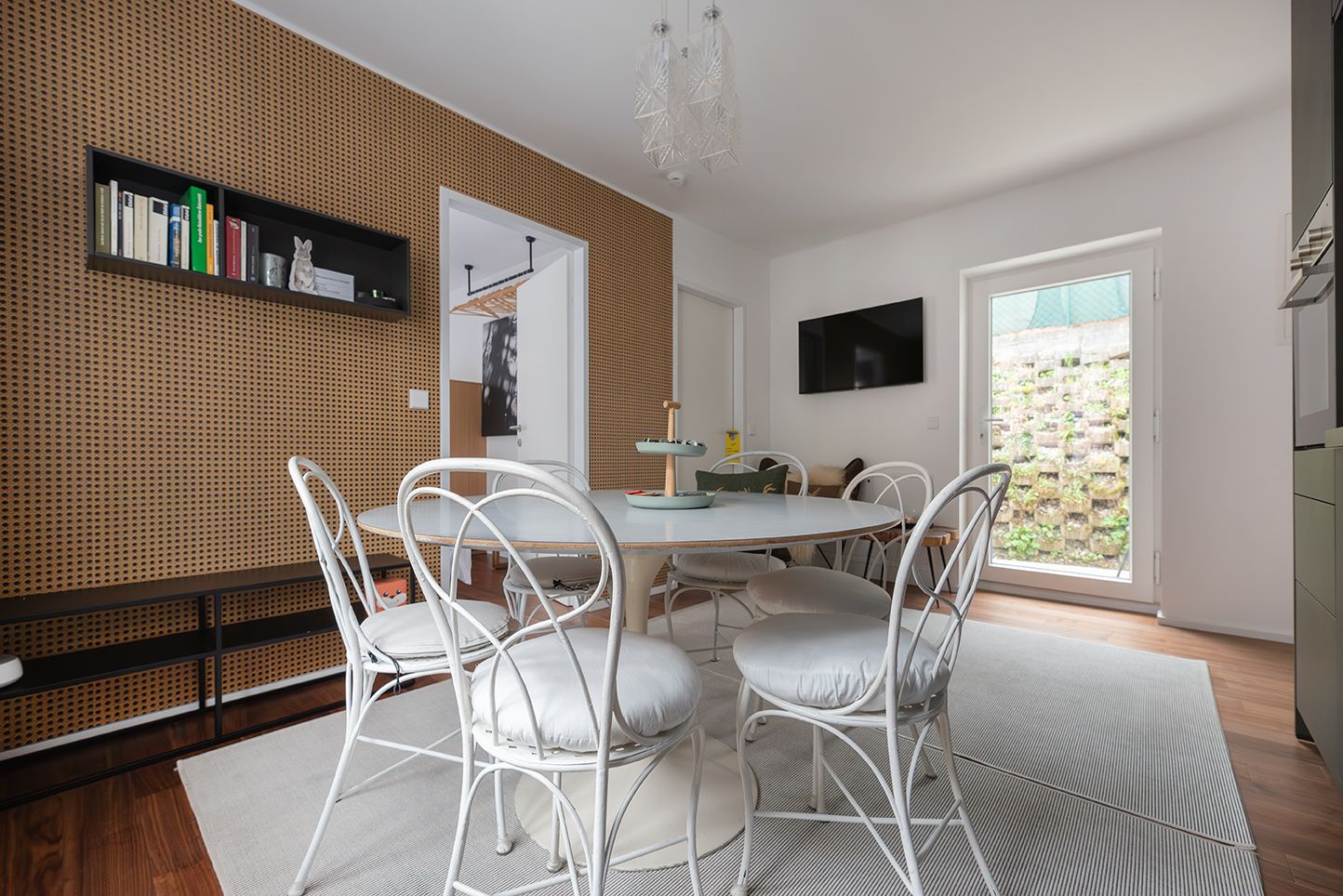 Modern dining area with round table and white chairs in front of a wooden wall.