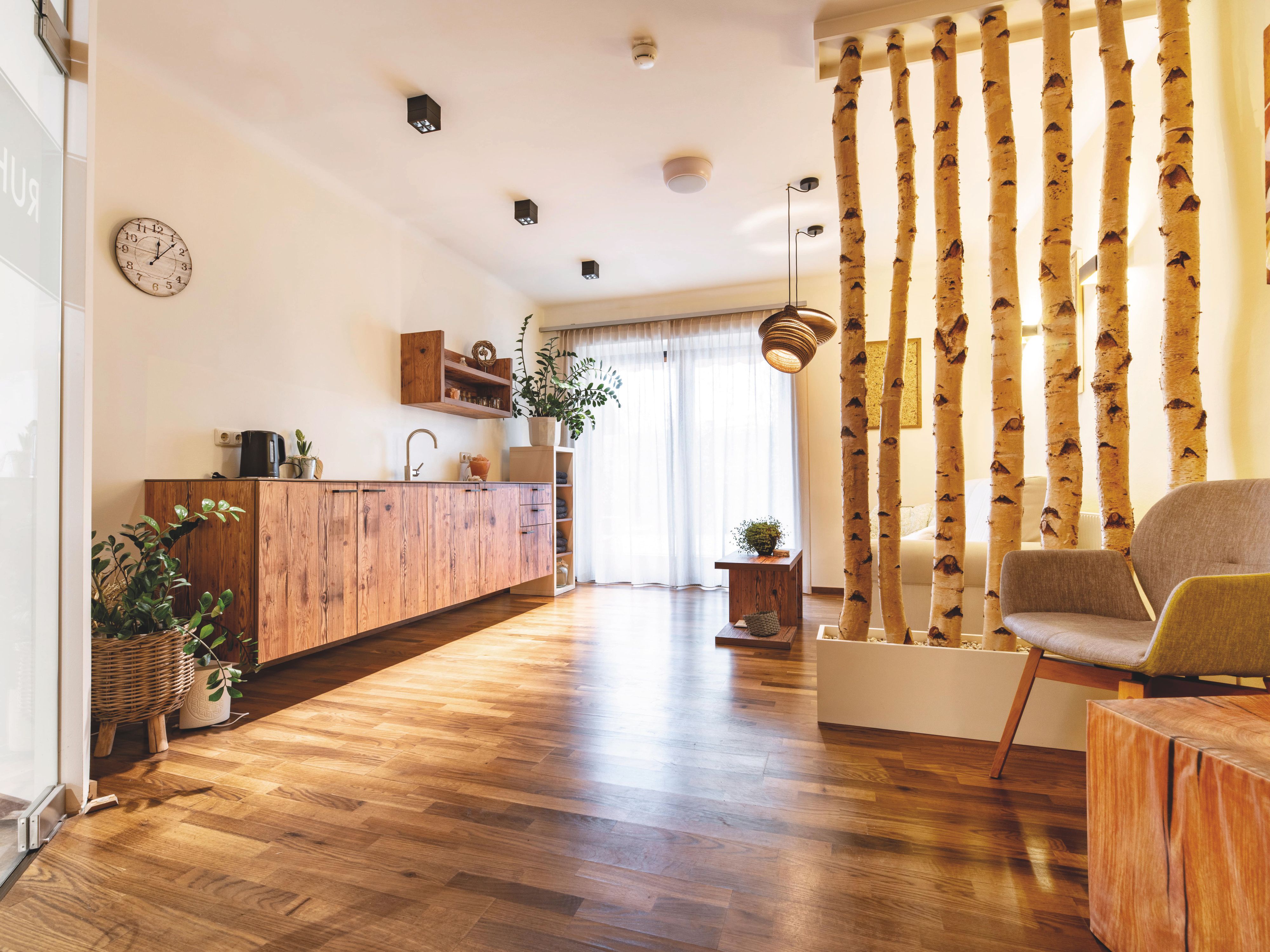 A modern room with wooden floors, seating areas, and birch logs serving as room dividers.