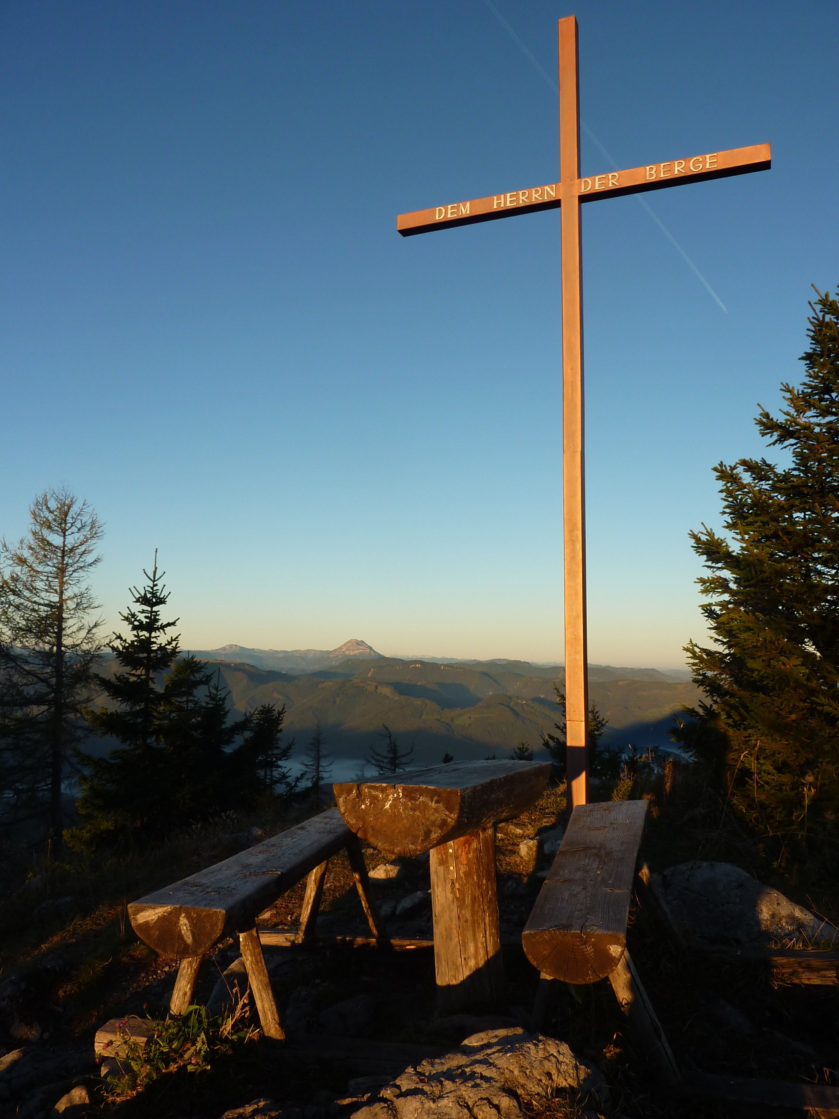 Summit cross on the Türnitzer Höger with wooden benches and mountain panorama in the background.