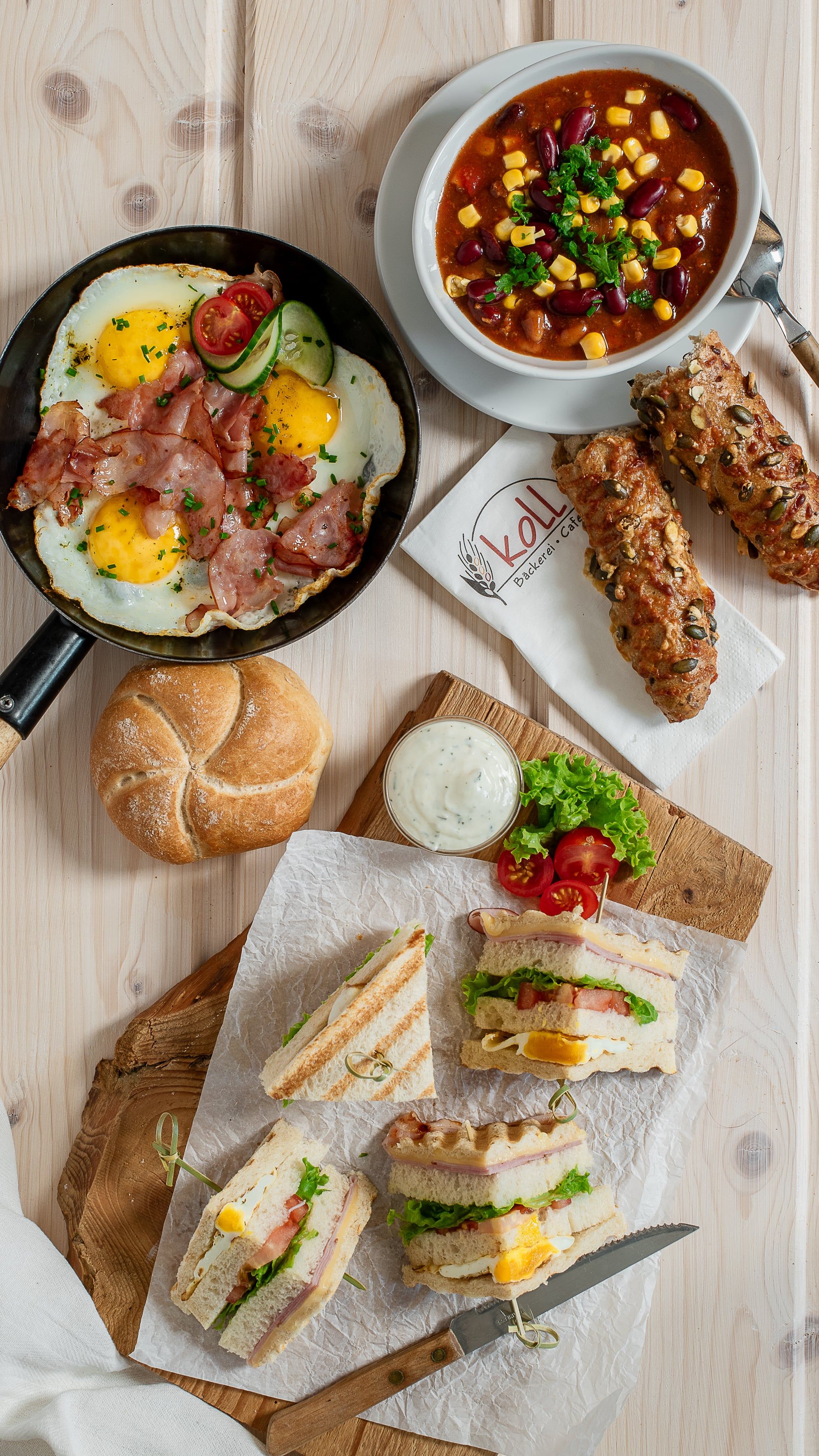 Various hot snacks on a table, including fried egg with bacon, soup, sandwiches and rolls.
