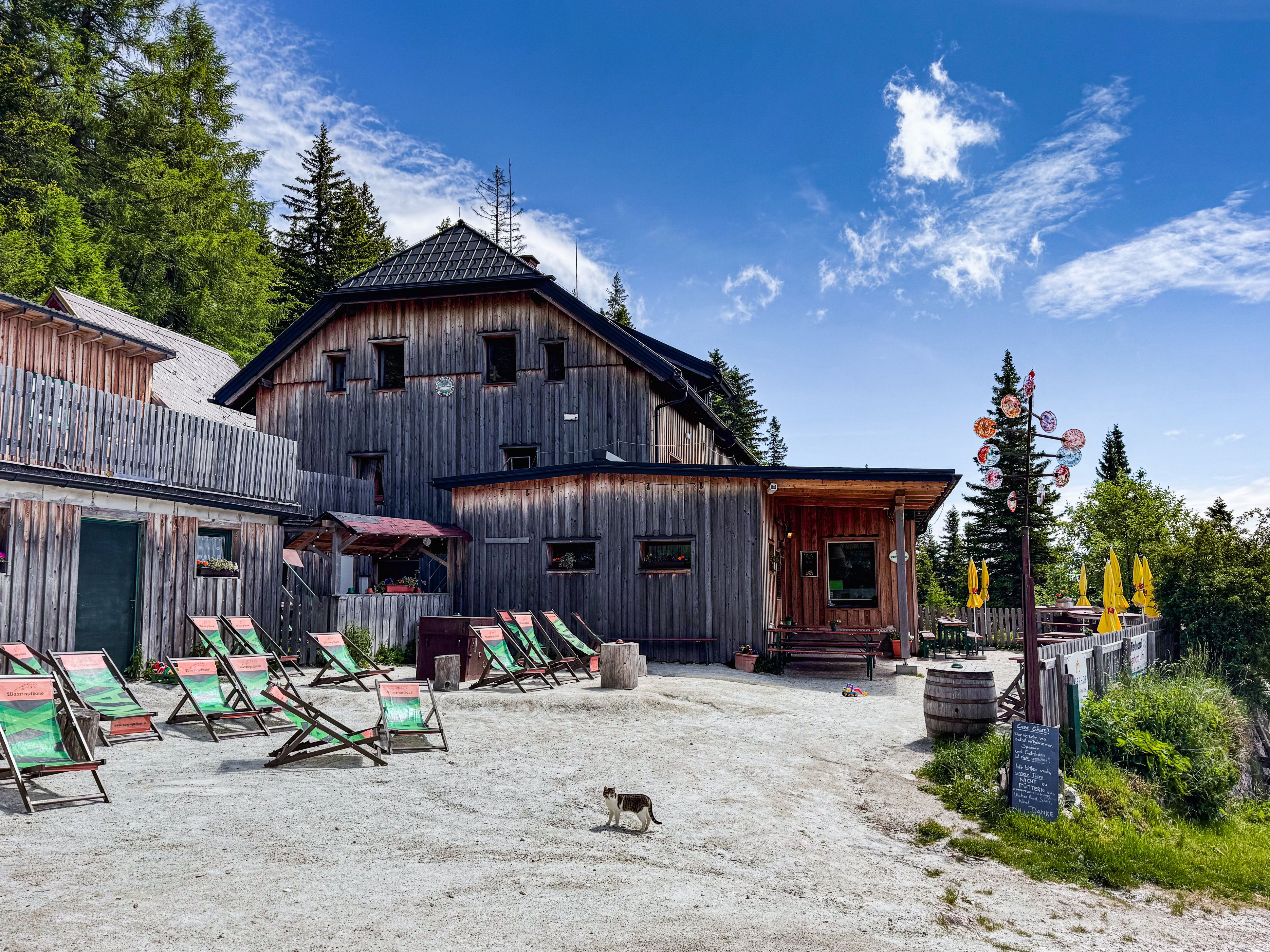 A rustic wooden building in a mountain landscape with sun loungers and parasols in the foreground.