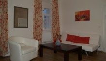 Living room with white armchair, sofa, wooden table and red accents.