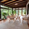 A conservatory with wooden floor, rattan furniture and lots of plants. Large windows offer a view of green nature.