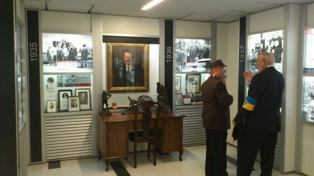 Interior view of a museum with two people in front of historical exhibits and photos.