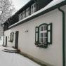 A snow-covered house with green shutters and guttering.