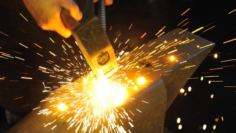 A blacksmith strikes red-hot metal on an anvil with a hammer, sparks fly.
