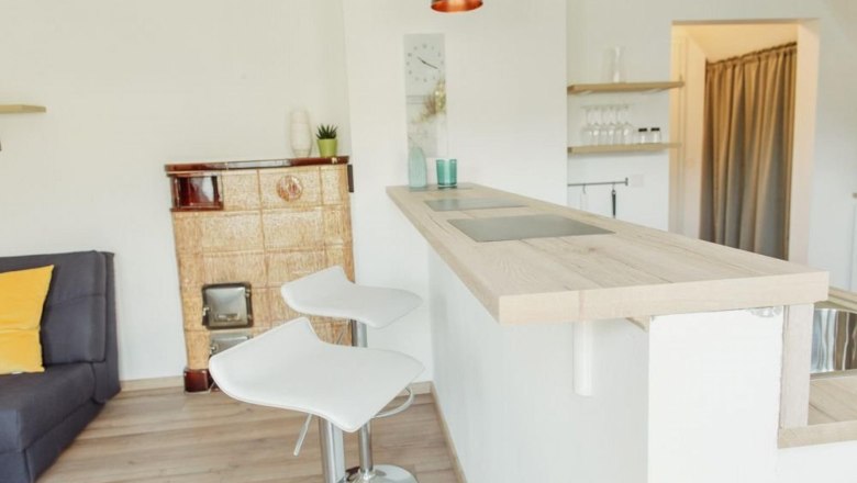 Modern kitchen with bar counter, two white bar stools and an old oven.