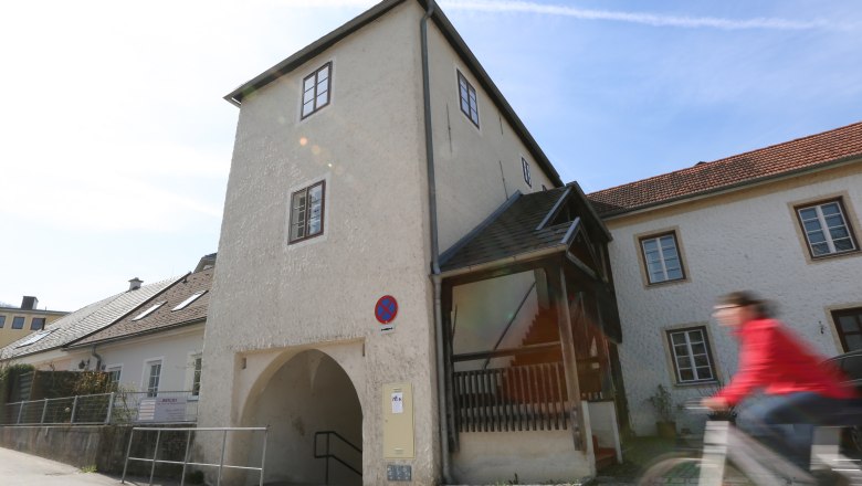 A historic building with an archway and a person on a bicycle in the foreground.