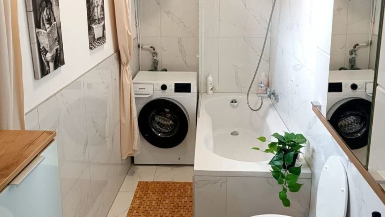 Modern bathroom with bathtub, washing machine and plants.
