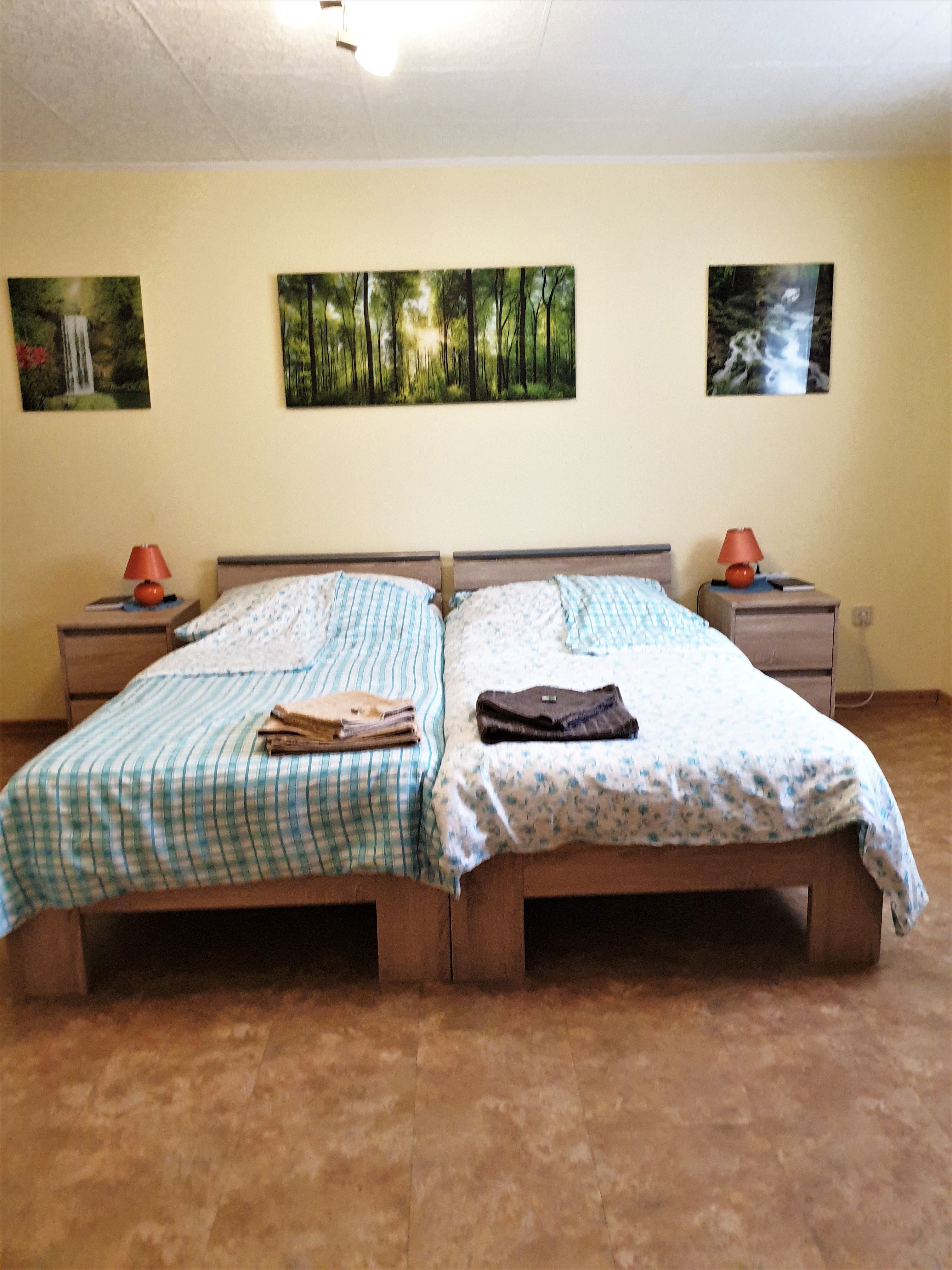 Bedroom with two single beds, bedside tables and forest landscape pictures on the wall.
