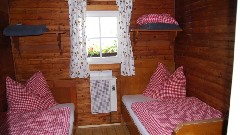 Wood-paneled room with two single beds, red and white checkered bedspreads and a window with flower curtains.