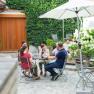 Group of people sitting at a table in a leafy courtyard with a parasol.