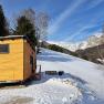 Small wooden house on a snow-covered hill with a mountain landscape in the background.