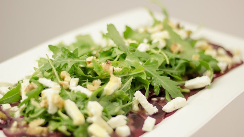 A plate with rocket, cheese and nuts on thin slices of meat.