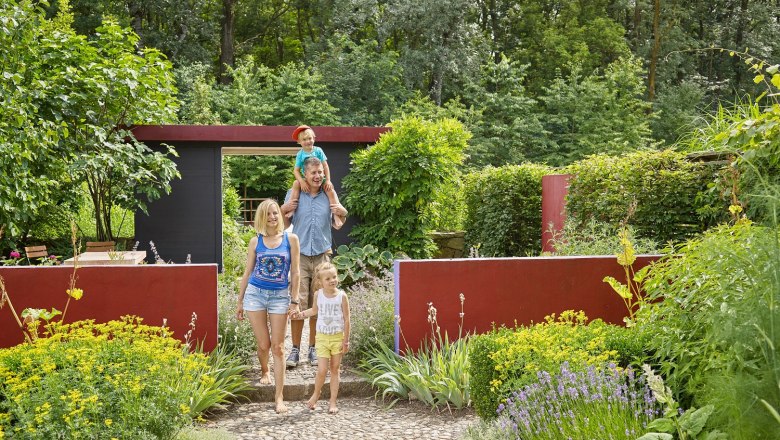 Family walks through a garden with colorful flowers and green bushes.