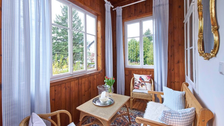 Top 1 - Conservatory, © VP FeWo OG A cozy winter garden with wooden walls, wicker furniture, blue curtains and a table with candles and flowers.