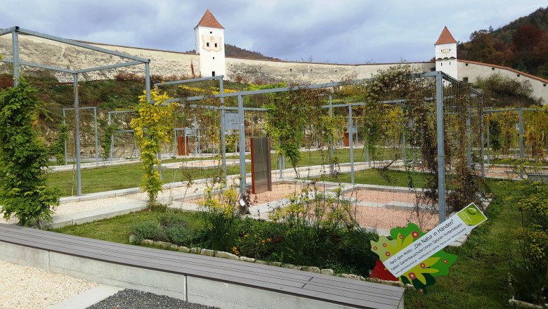 Gardens of the Aggsbach Charterhouse with metal structures and towers in the background.