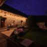 An illuminated courtyard at night with stone walls, wooden benches and blooming flowers.