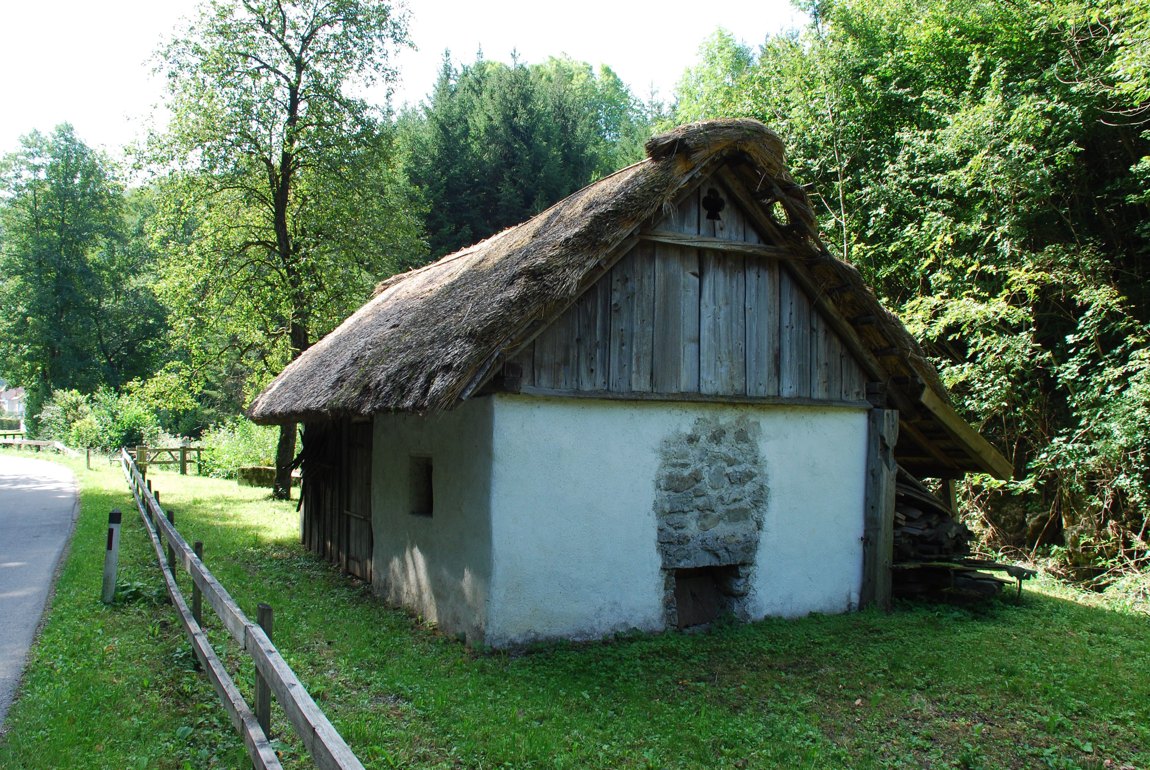 A traditional thatched cottage in a rural setting, surrounded by trees and meadows.