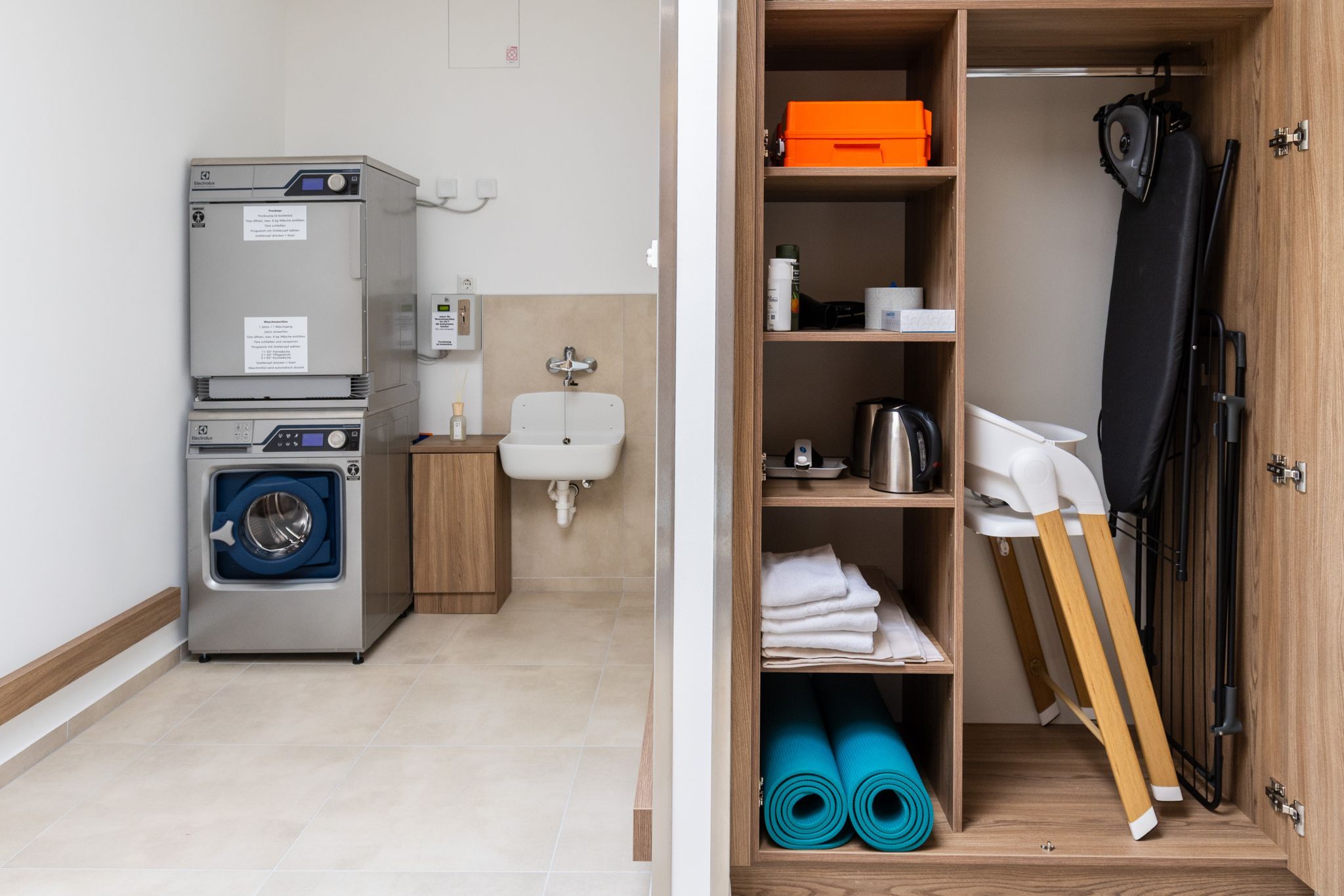 A laundry room with a washing machine, dryer, sink, and a cabinet containing household items such as an ironing board and a kettle.