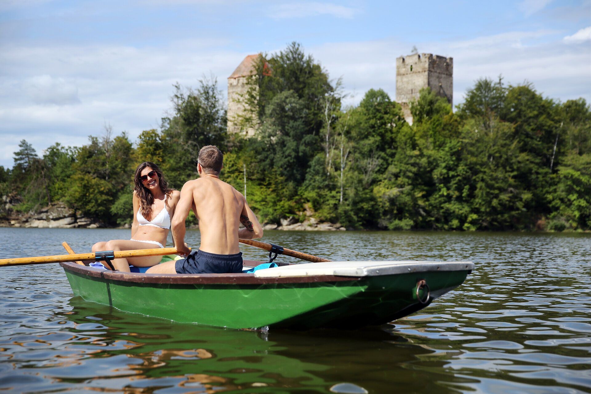 A sunny day at the Ottenstein Reservoir is perfect for a romantic boat ride. The gentle waves reflect the surrounding forests and the majestic ruins, while the laughter of the two visitors fills the peaceful atmosphere.