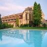Historic building with pool in the foreground, surrounded by trees and garden.