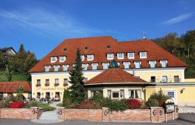 Exterior view of a yellow country hotel with a red roof and garden.
