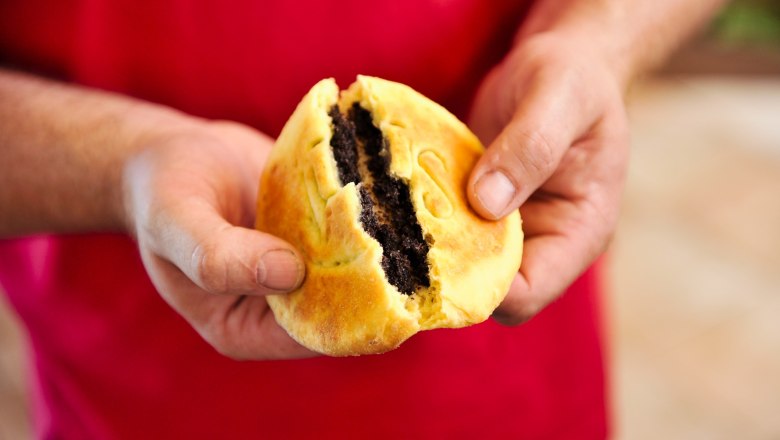 Person holding a broken pastry with poppy seed filling.