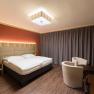 Modern hotel room with double bed, wooden furniture and curtains.