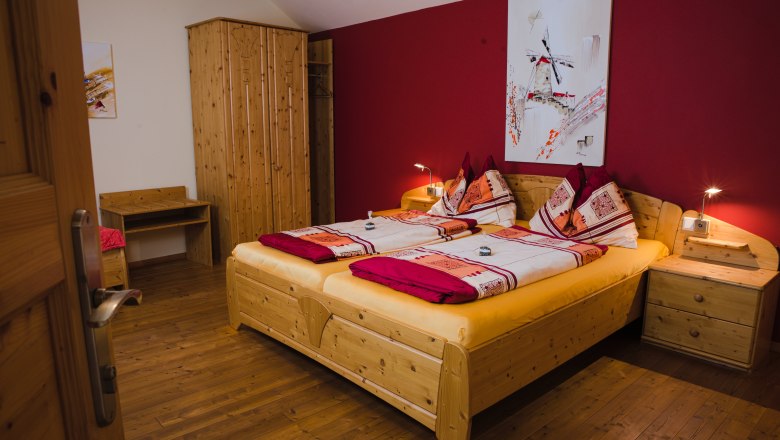 Cozy guest room with double bed, wooden furniture and red wall.